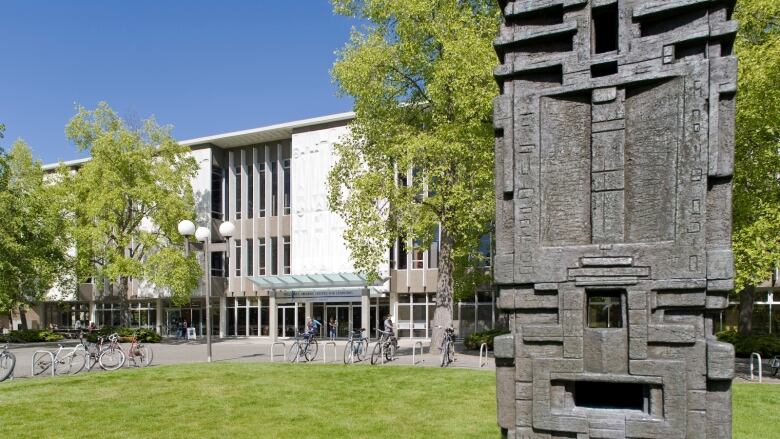 An image of a totem pole in front of a modern campus building, with bicycles in front of it.