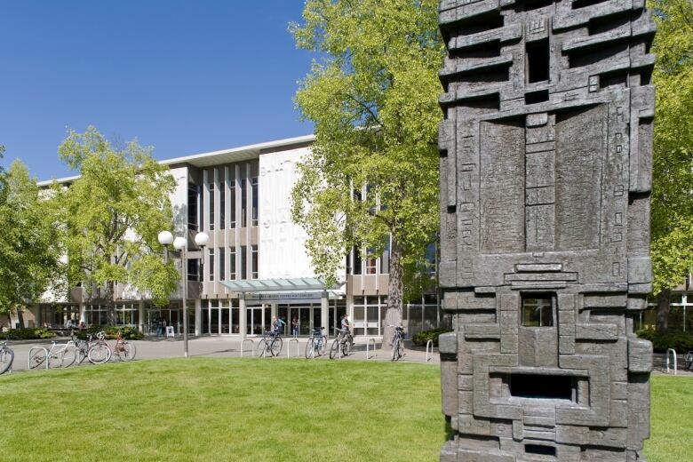 An image of a totem pole in front of a modern campus building, with bicycles in front of it.