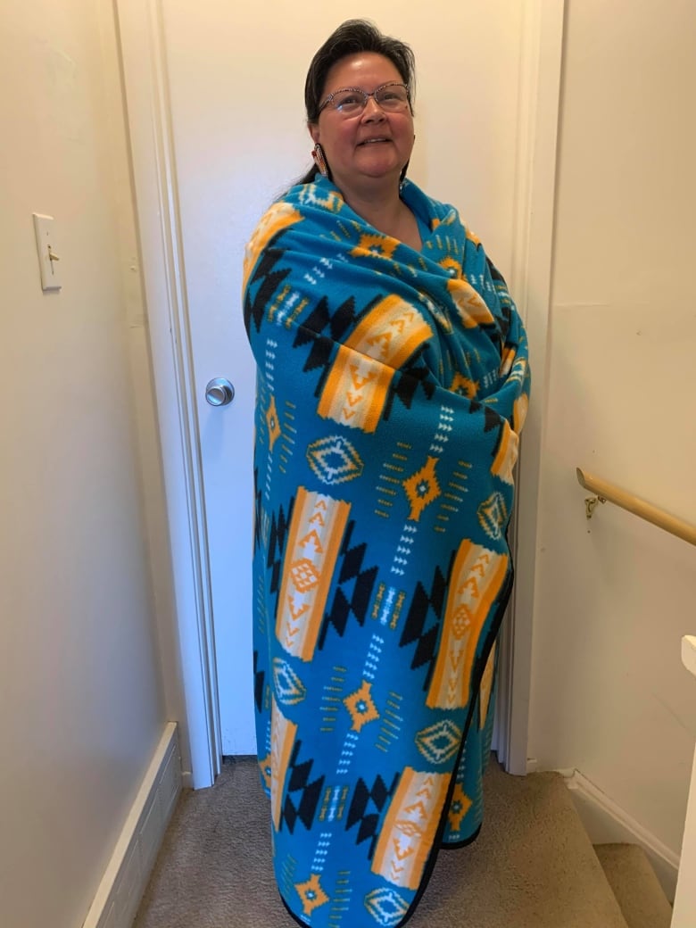 A smiling woman wrapped in a tribal printed, blue and yellow blanket.