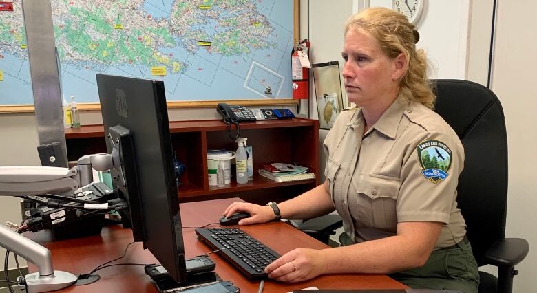 A woman sits in front of a computer with a map of Nova Scotia on the wall behind her.