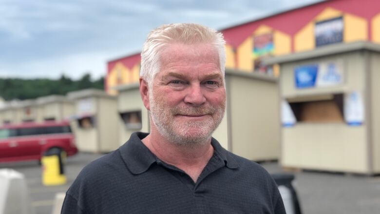 A man stands outside in a parking lot wearing a black polo shirt.