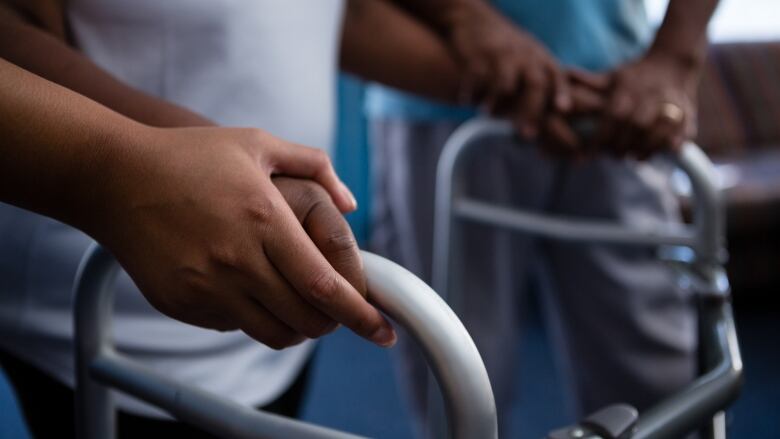 Cropped hands of nurse assisting woman in walking with walker at retirement home.