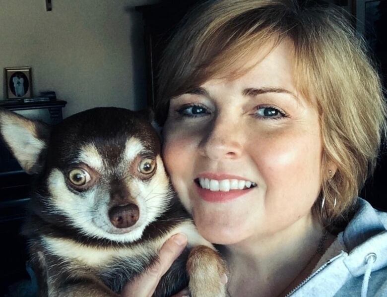 A woman holds a dog smiling.