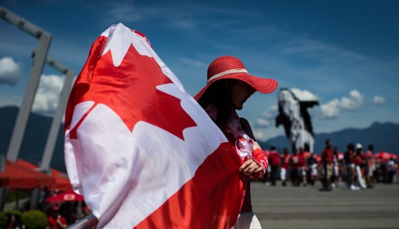 A woman in a red hat holds a Canada flag in front of Canada Place.