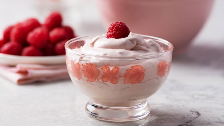 Closeup on a small glass bowl of pink mousse topped with a raspberry. 