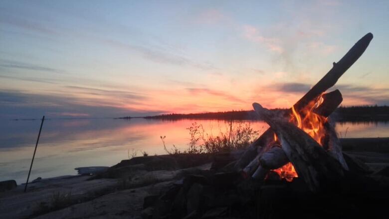 A bonfire burns with a sunset in the background. 