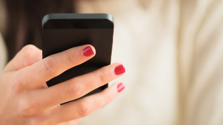 A person's hand holding a phone. The person has painted red nails.