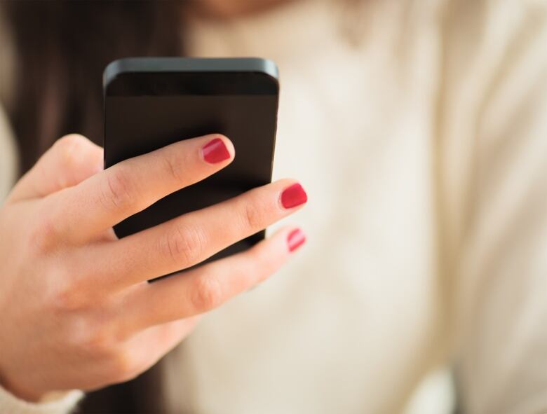 A person's hand holding a phone. The person has painted red nails.