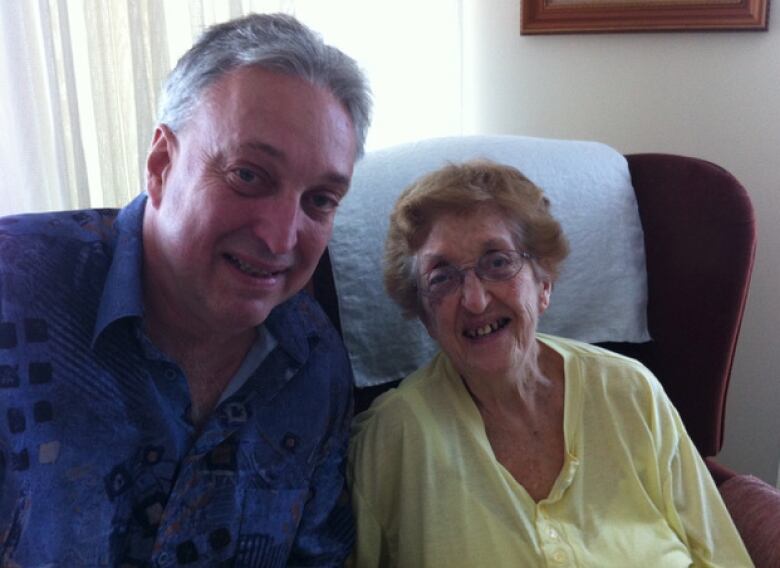 A portrait of a man and an elderly woman. Both are smiling at the camera.