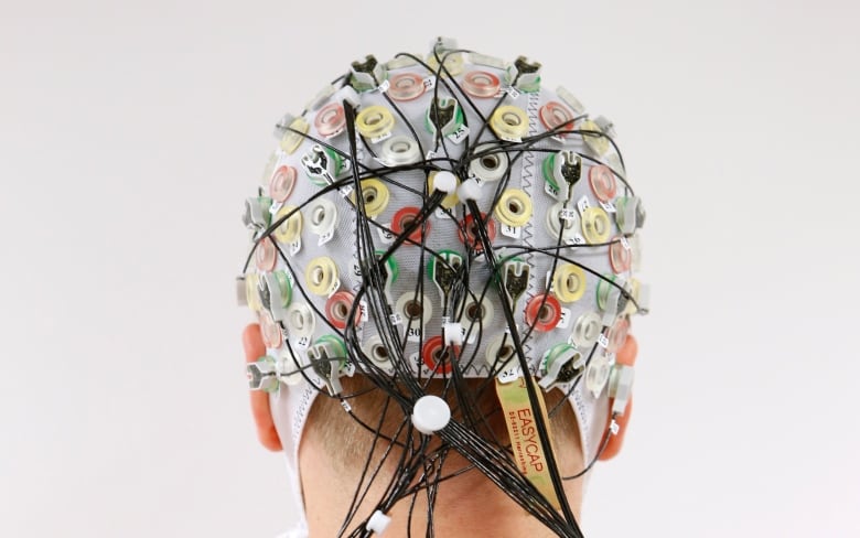 A skullcap covered in sensor nodes and wires is placed on a person's head.