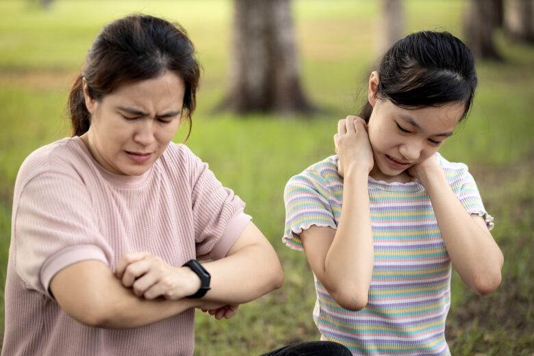 An Asian woman and girl scratch themselves because of mosquito bites.