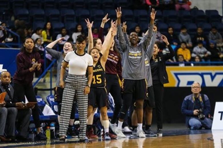 A woman looks at the action on a basketball court as a group of female fans surround her, cheering wildly.