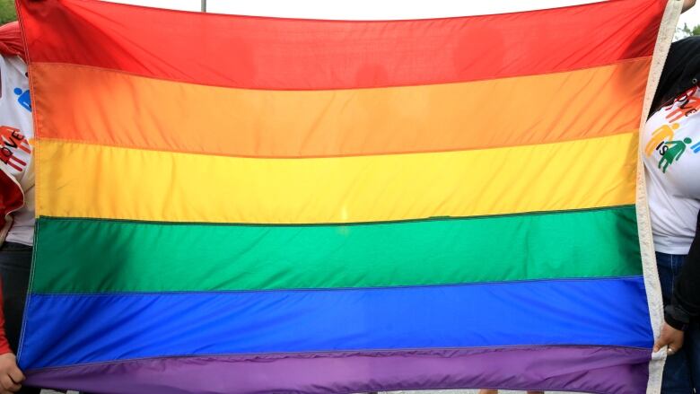 Unseen individuals on each side of the photo hold up a rainbow flag