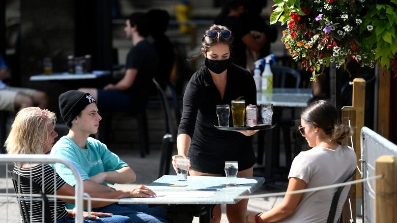 A server wears a mask as she brings drinks to patrons on a pub's curbside patio in the Byward Market in Ottawa, on Sunday, July 12, 2020, in the midst of the COVID-19 pandemic. 