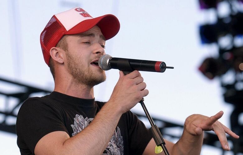 Man singing into microphone wearing T-shirt and trucker hat