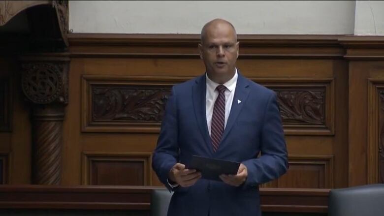 A man in parliament holding documents.