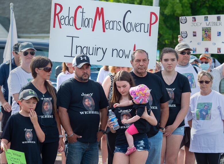 People in black T-shirts stand in front of picket signs at a protest.