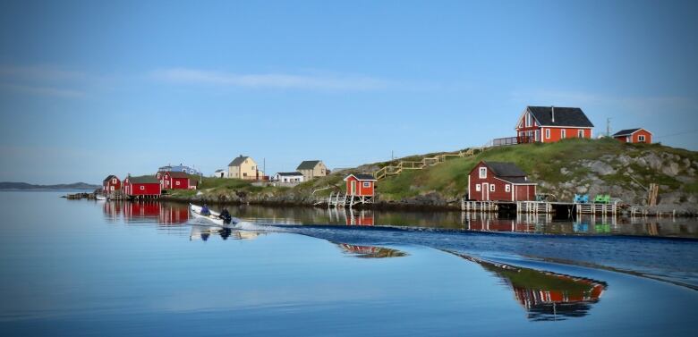 A scenic photo of a small Newfoundland outport showing two men riding in a boat on very calm waters.