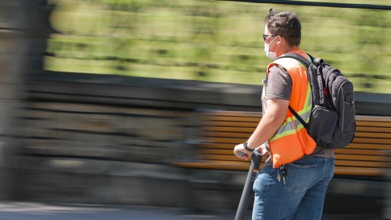 A person is riding an e-scooter and the photo has motion blur to indicate the e-scooter is in motion.