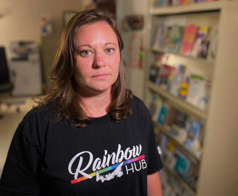 A woman wearing a rainbow tshirt looks at the camera. 