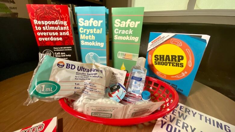 A basket with syringes and other supplies sits on table with pamphlets about safe drug use. 