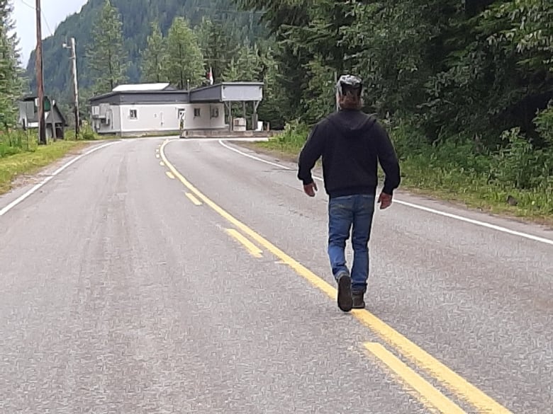 A man walks on a road towards a building.