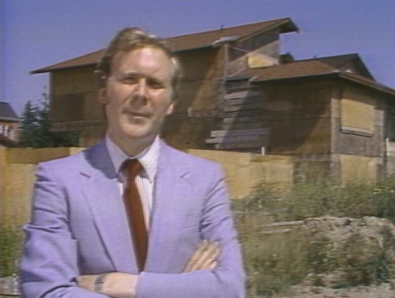 Reporter with crossed arms in front of house with boarded-up windows