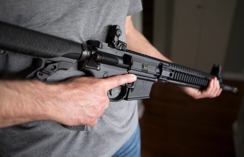 A man holds an AR-15 rifle.