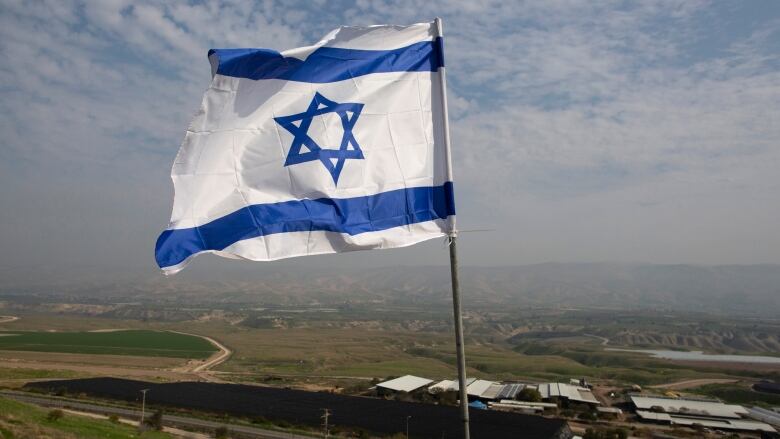 blue and white Israeli flag is scene in the foreground with landscape visible in background