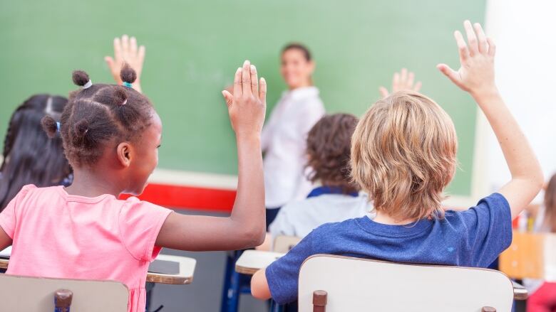 A number of children raise their hands in a classroom.