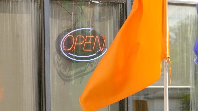 An orange flag hangs outside a business with a neon 