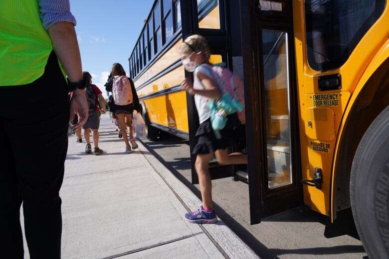 A student waring a respiratory mask leave a school bus at the start of a school year.