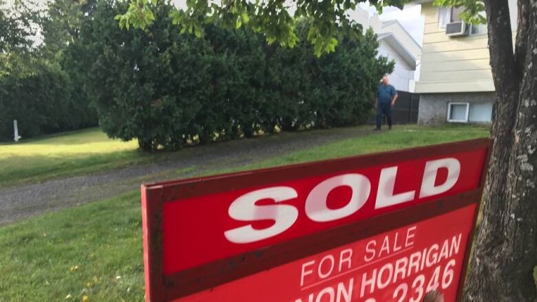 A 'SOLD' realtor sign outside a large house.