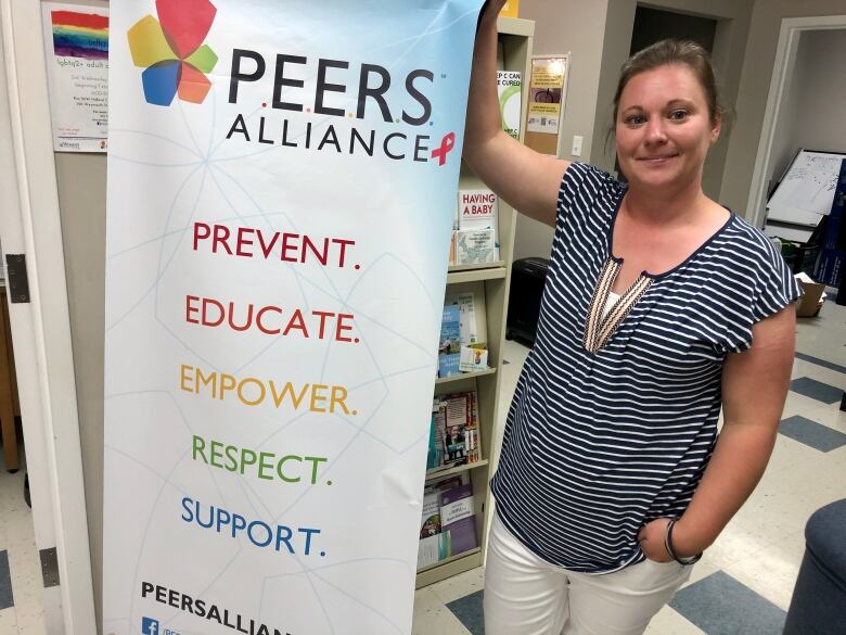 Young woman stands next to tall banner that reads: PEERS Alliance. Prevent, Educate, Empower, Respect, Support.