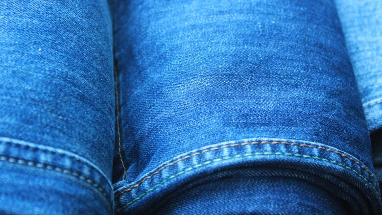 A close-up shot of three pairs of blue jeans, rolled and stacked side by side