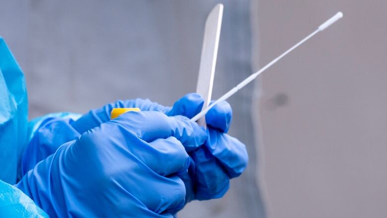 a gloved hand holds a long cotton swab