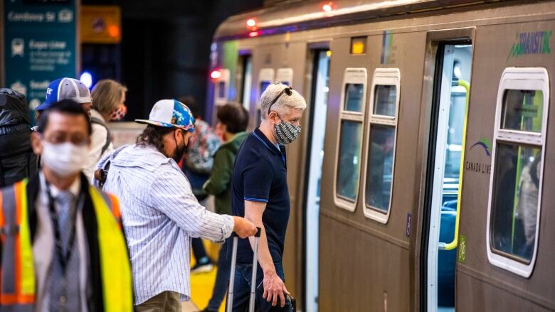 A group of people wearing masks enter a SkyTrain.