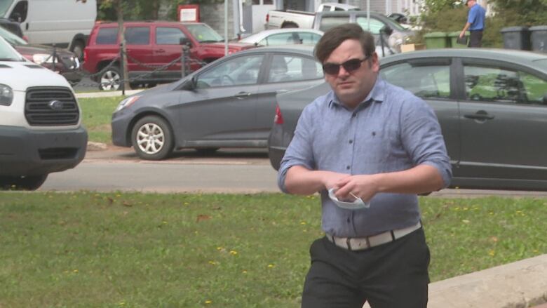 A man in a blue shirt and sunglasses walks into a courthouse.