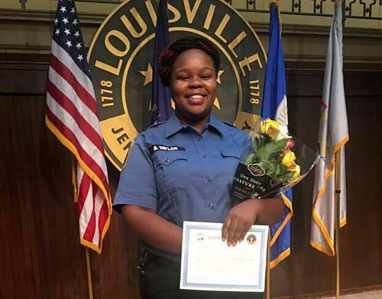 A person in uniform smiles and poses for a photograph while holding flowers and a certificate.