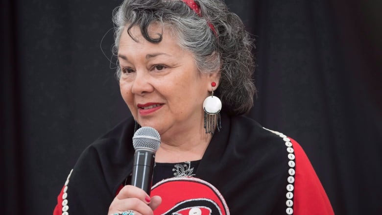 A woman in red and black speaks into a microphone.