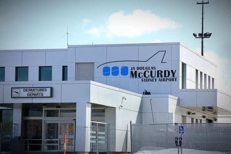 A sign on the outside of an airport building shows a picture of an airplane and the name J.A. Douglas McCurdy Sydney Airport.