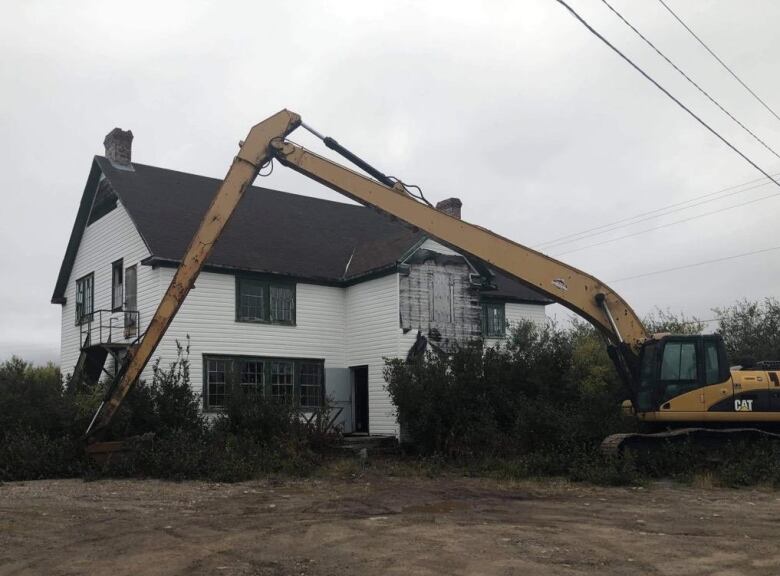 An excavator in front of an old white three-storey building.