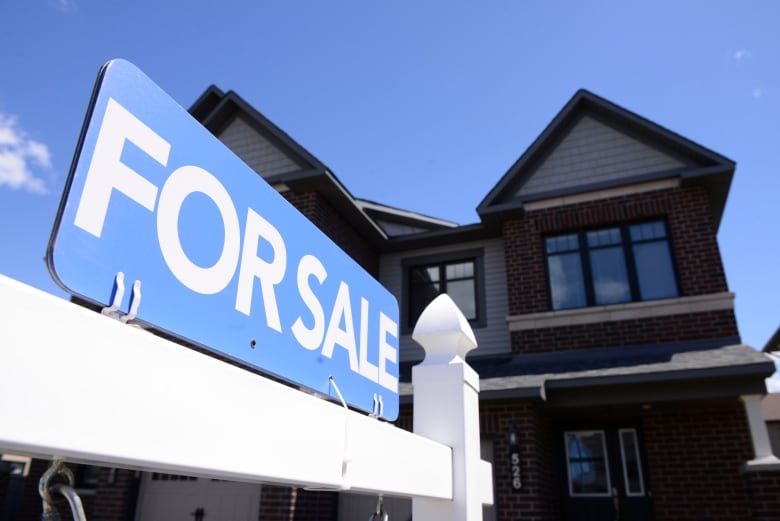 A blue and white for sale sign in front of a red brick house