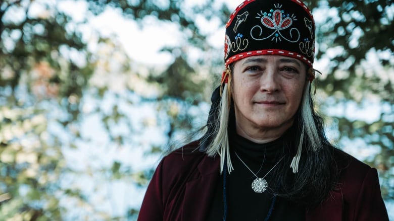 A woman wearing Indigenous regalia stands outside.