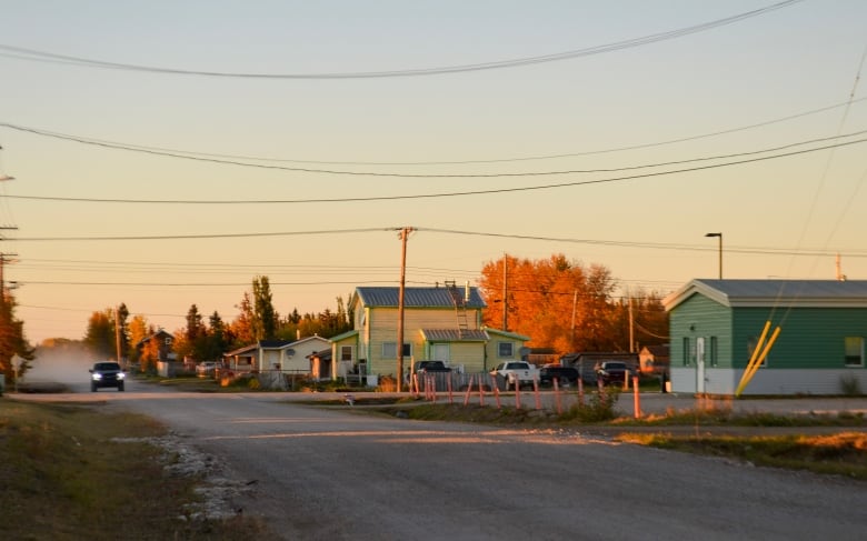 A rural road with buildings on the right, and a vehicle in the distance driving toward the camera.