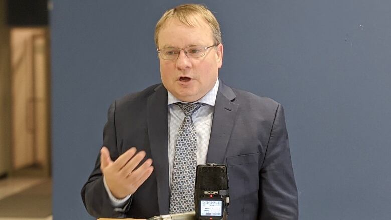 A man in a suit speaks before a microphone.