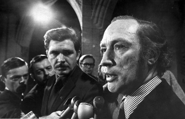 Prime Minister Pierre Elliot Trudeau speaks with reporters in this black and white image.