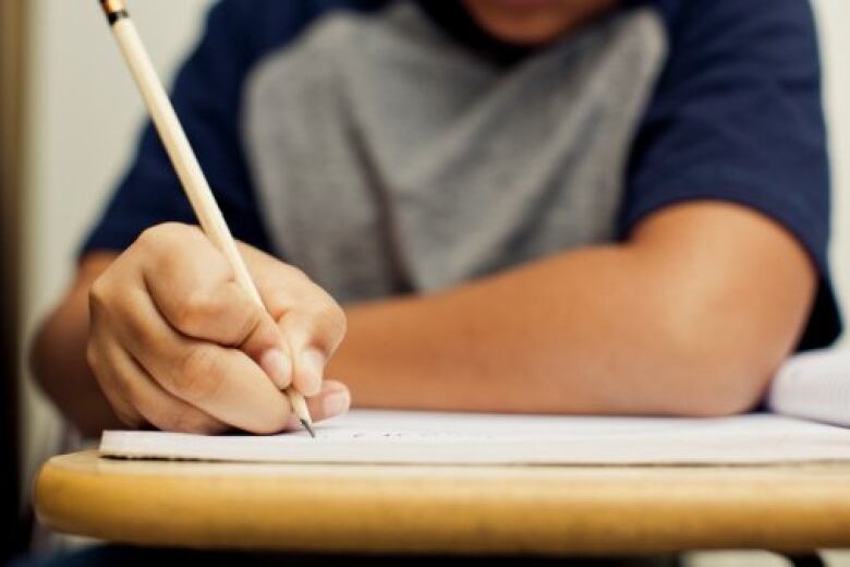 A close-up of a male student sitting at a desk holding a pencil over a piece of paper