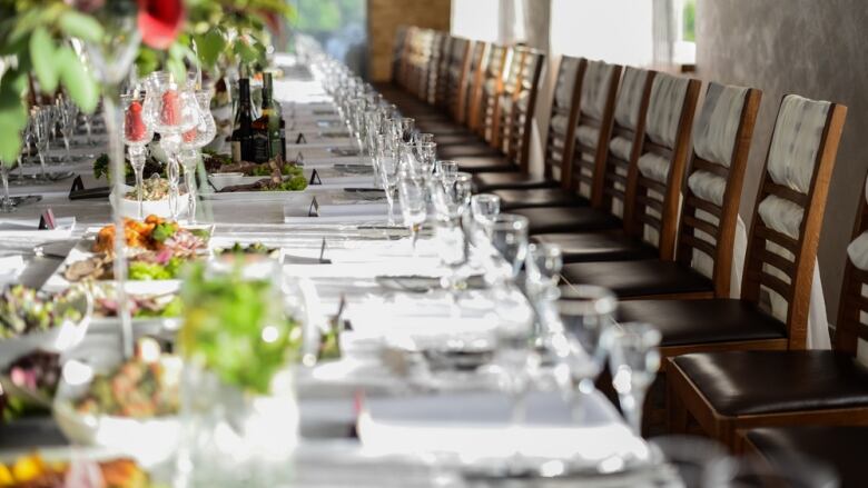 A long table with chairs lined up next to it. On the table, there are glasses and cutlery, as well as plates with food and different decorations.