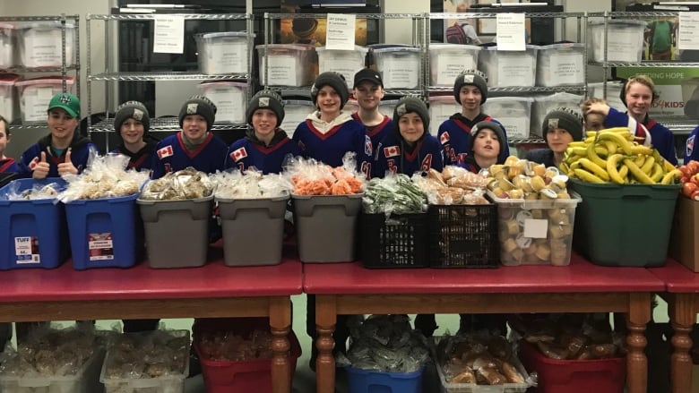 A row of kids stands behind a row of bins filled with food.